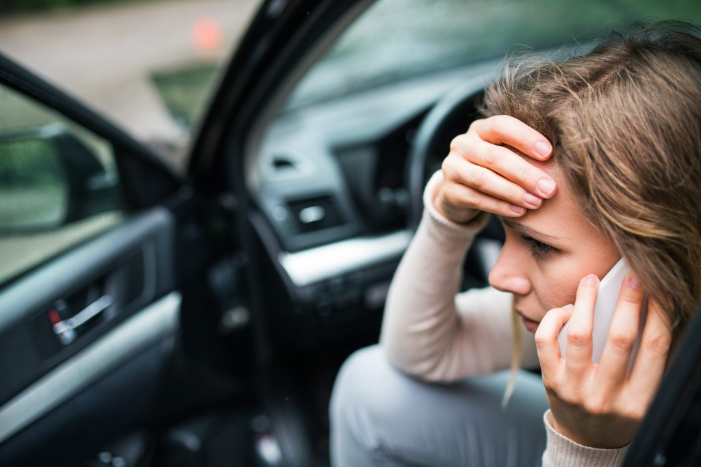 Young woman in the damaged car after a car accident, making a phone call.