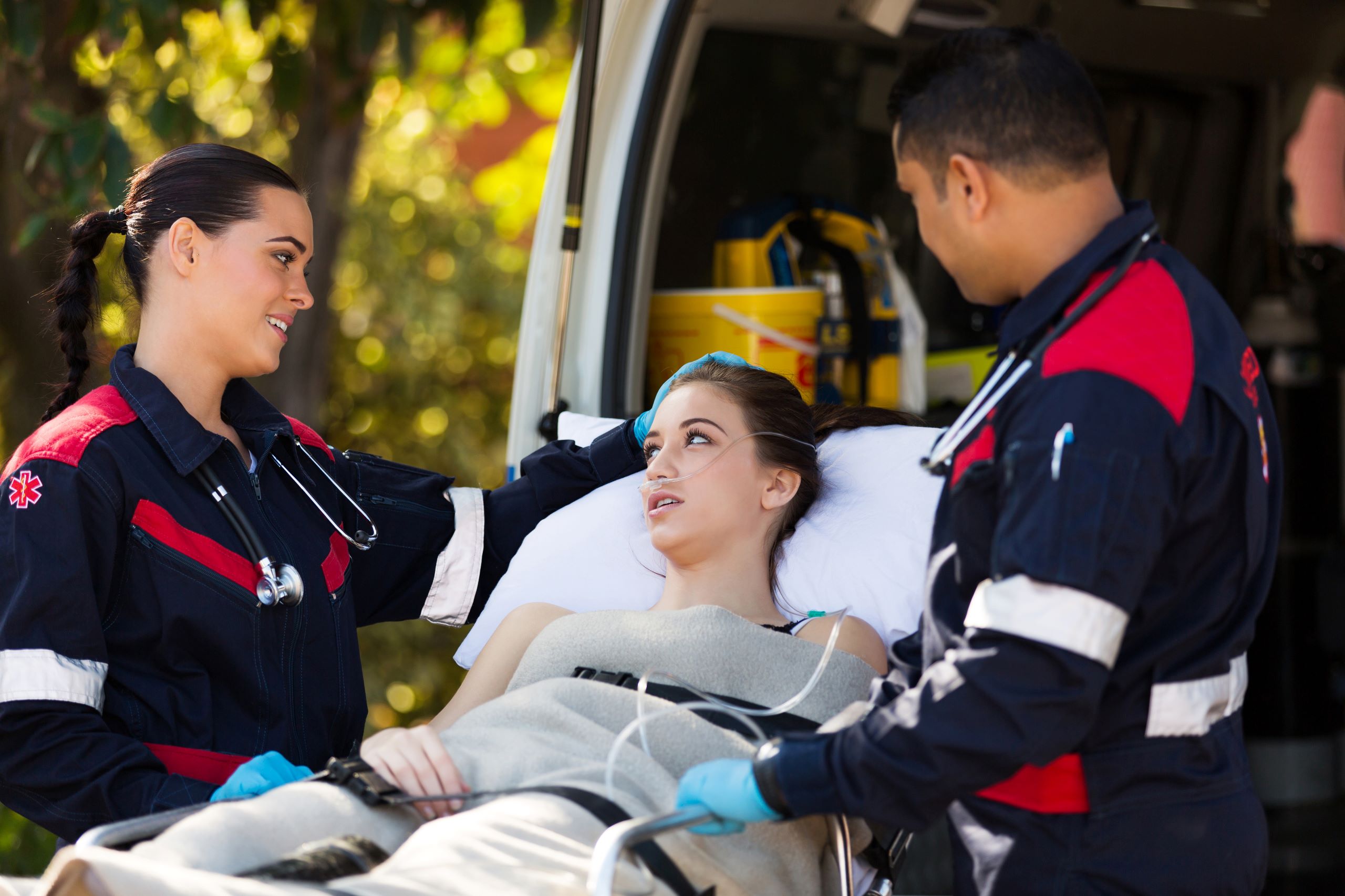 Woman on a gurney speaking with emergency medical technicians outside of an ambulance.